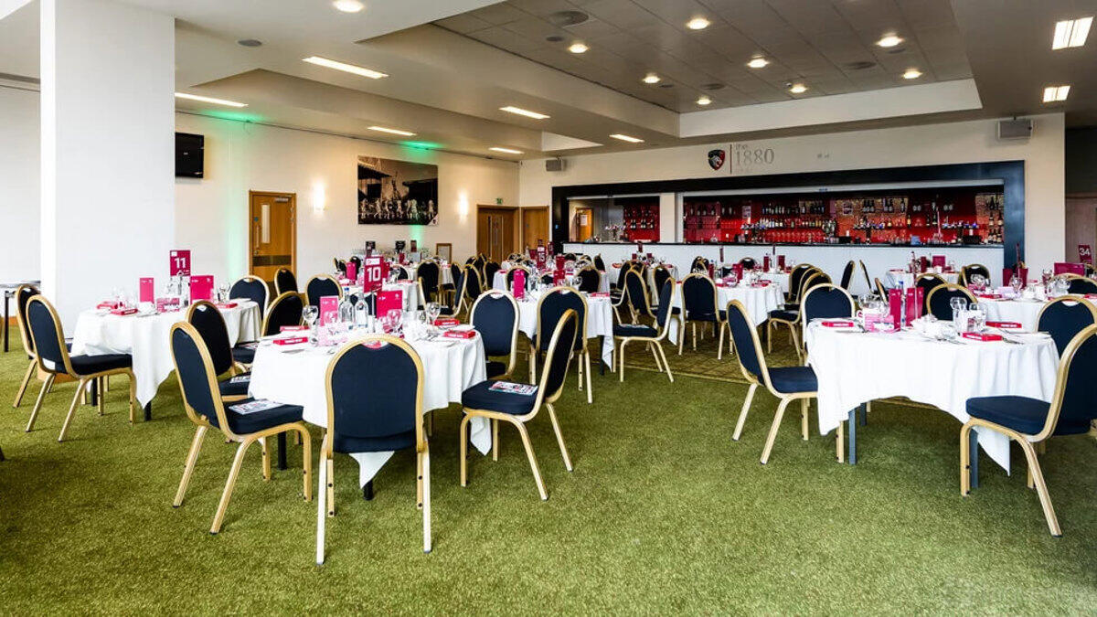 An event space with round tables covered in white linens and a bar along the wall at Leicester Tigers’ 1880 Club.