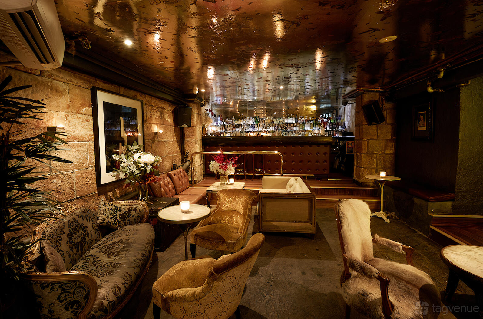A function room in a bar with velvet armchairs, exposed stone walls, and a mirrored ceiling at Tatler Sydney.