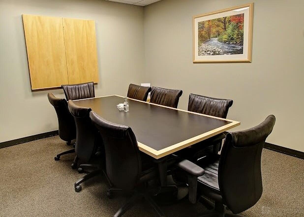 A meeting room with a rectangular table, eight leather chairs, and framed wall art at Intelligent Office - Boston.
