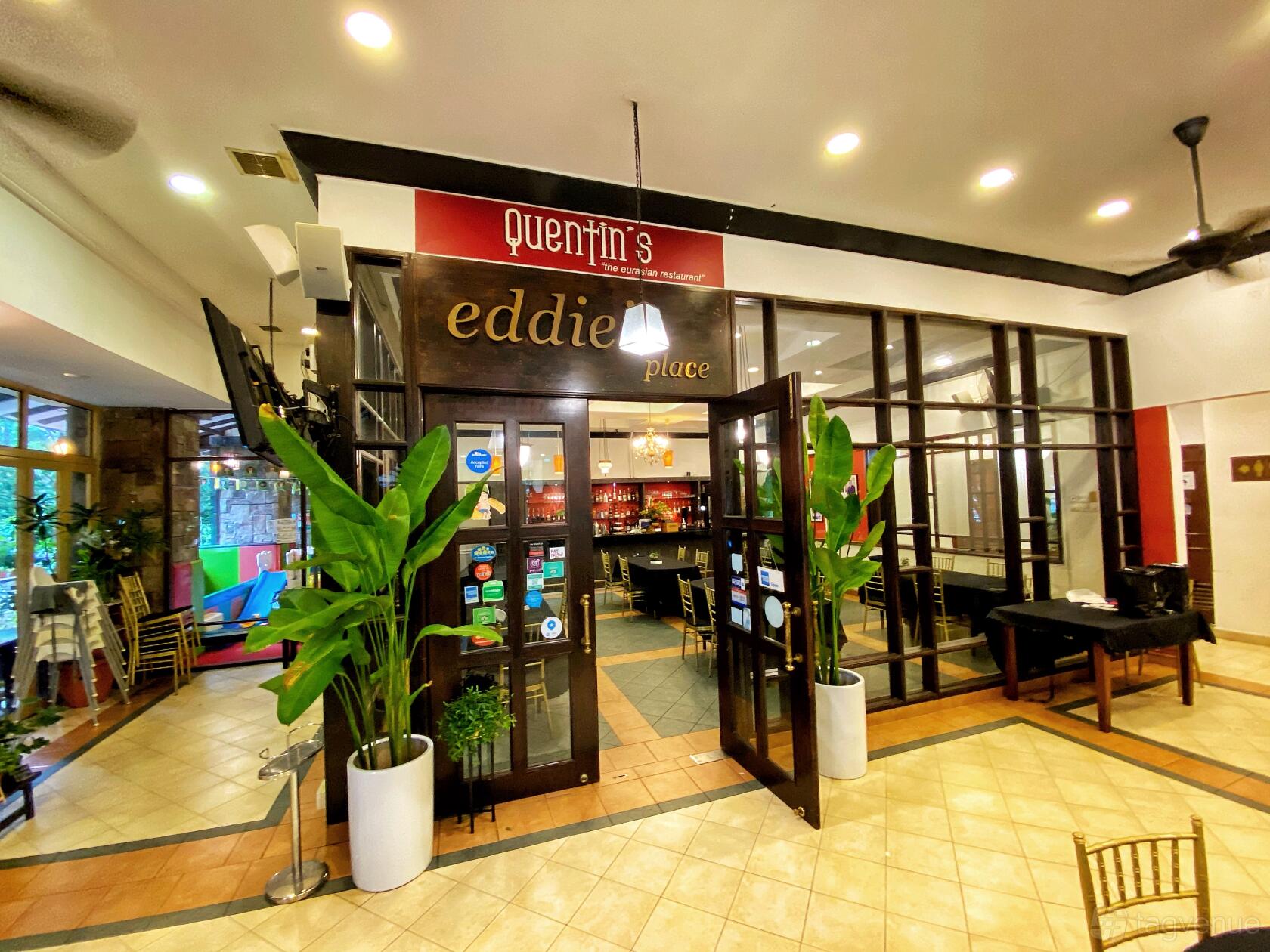 A restaurant entrance with glass-panel doors, potted plants, and overhead spotlights at Quentin's the Eurasian Restaurant.