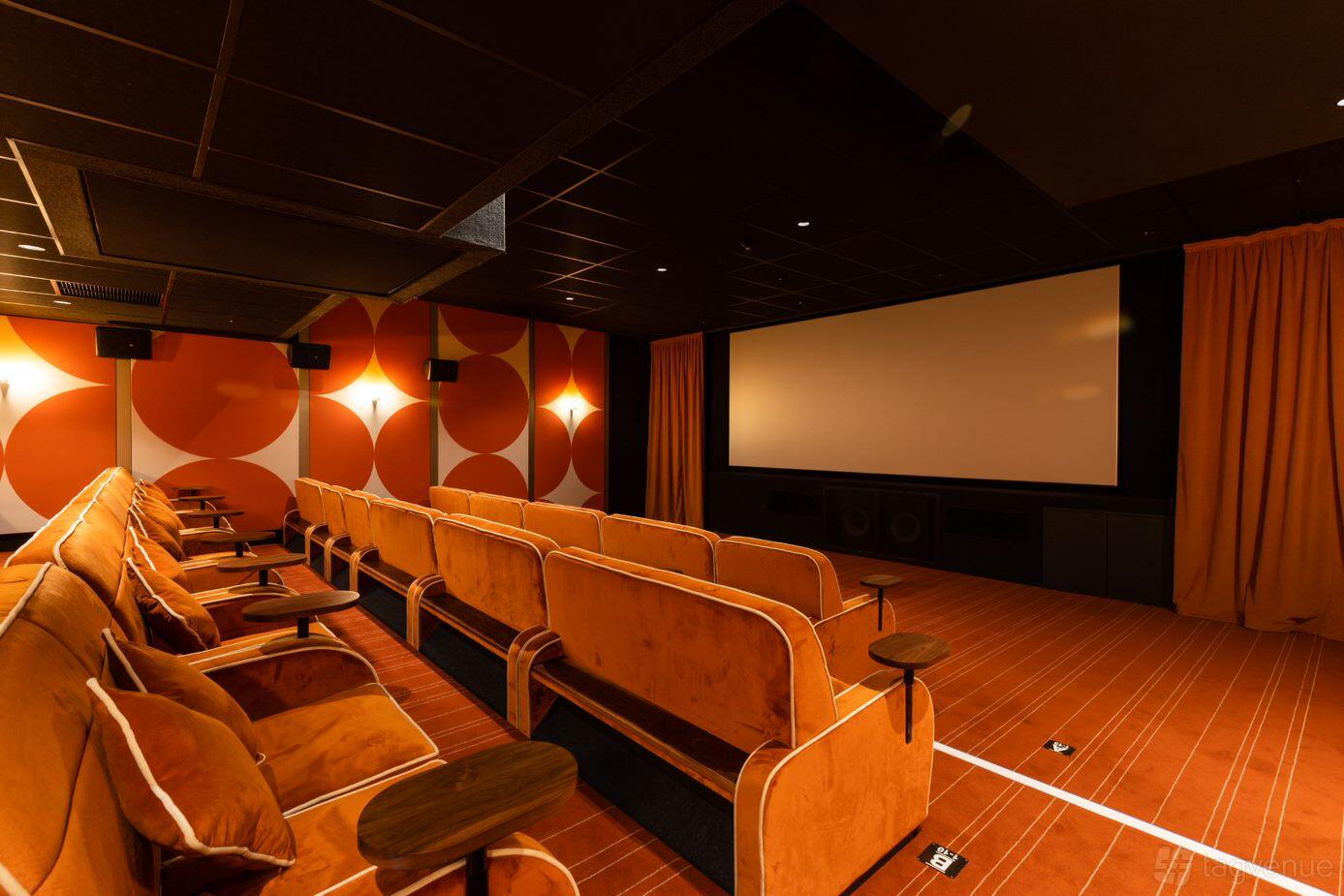 An auditorium with plush orange velvet seating, wood armrests, and retro patterned walls at Everyman Edinburgh.
