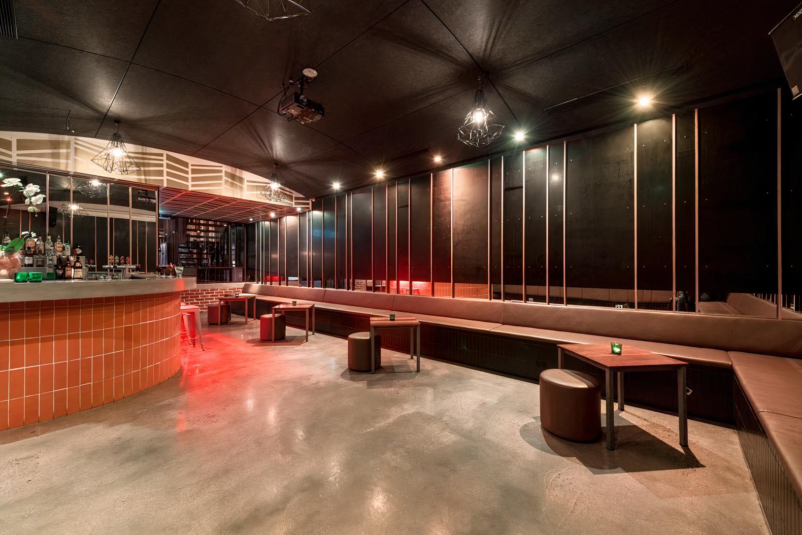 A function room with a curved tiled bar, long bench seating, round tables, and ambient lighting at Arcadia Hotel.