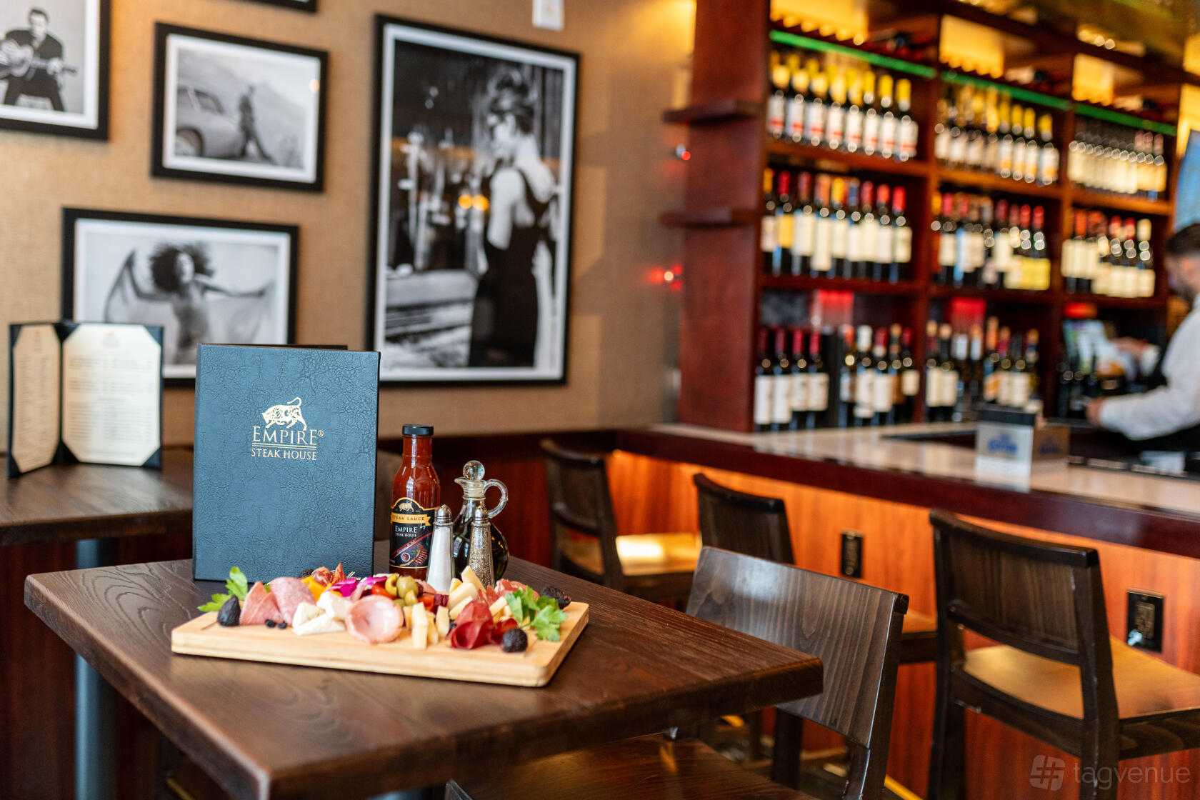 A restaurant with wood tables, a charcuterie board, and a wine display wall at Empire Steak House Times Square.