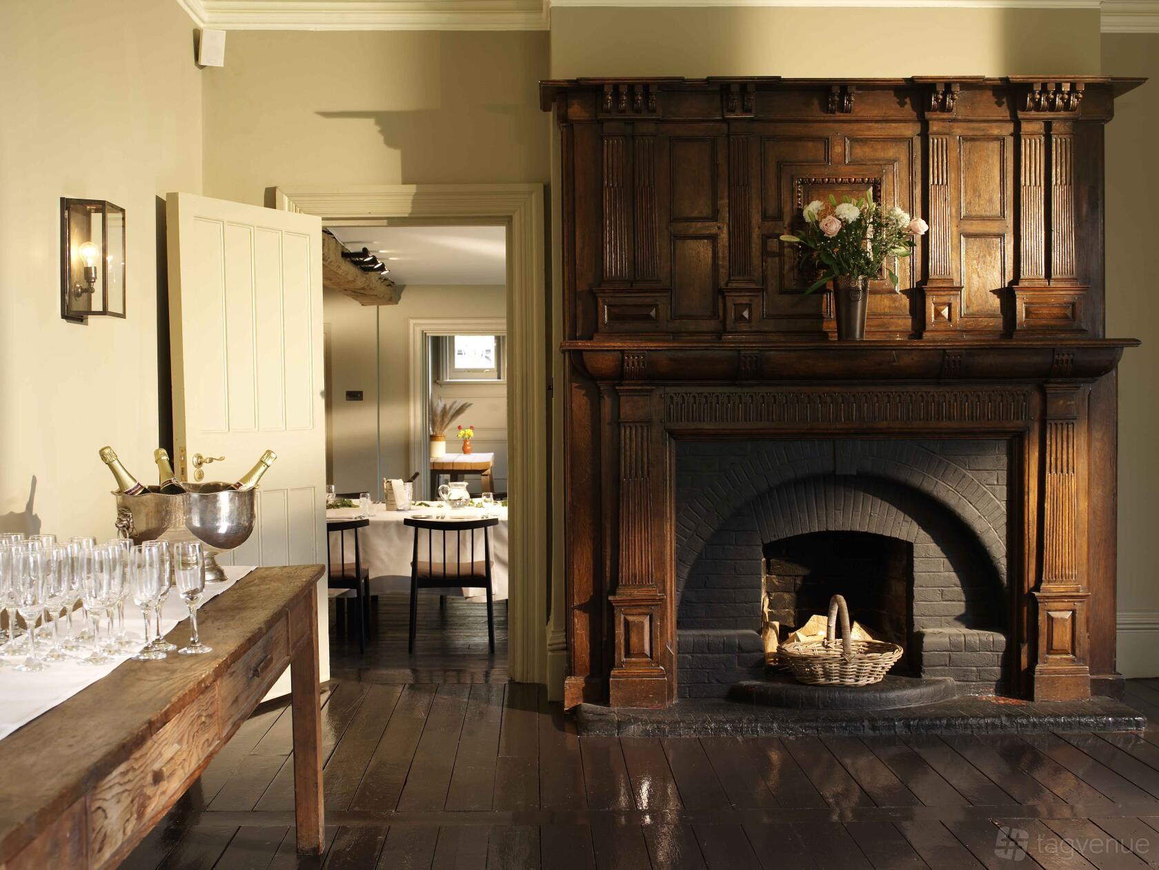 A hotel room with a large carved wooden fireplace, basket of logs, and champagne glasses at The Olde Bell.