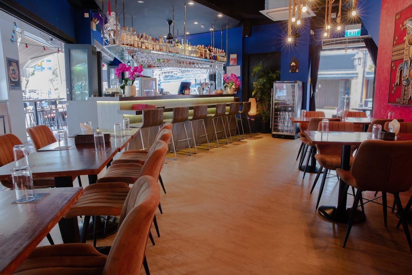 A restaurant with a long bar, upholstered dining chairs, pendant lighting, and glassware at Drunk Skunk Bar & Bistro.