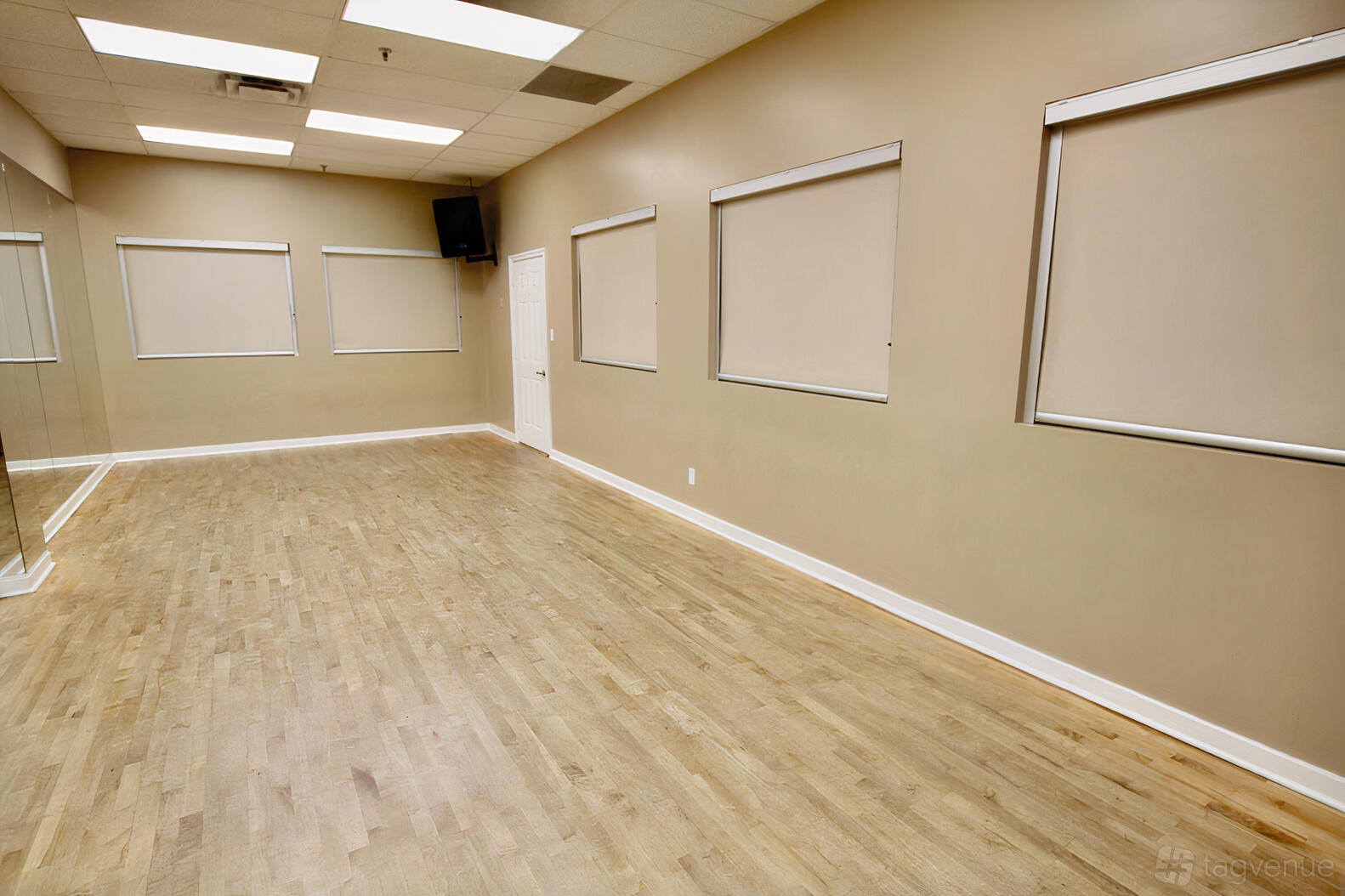 A rehearsal studio with mirrored walls, wood flooring, and covered windows at ViBE Dance Studio.