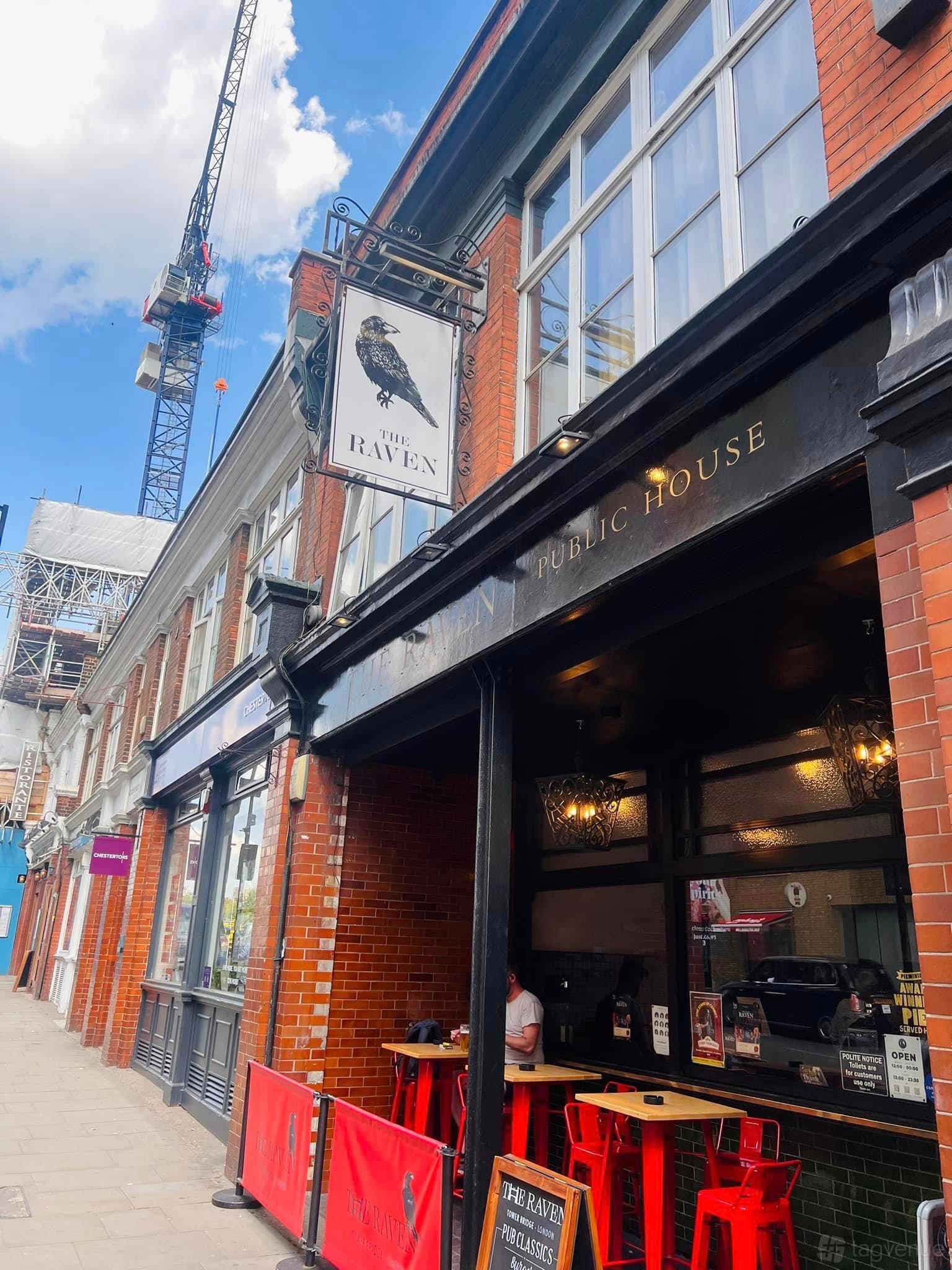 A pub with a traditional brick exterior, black signage, and hanging lanterns at The Raven Tower Bridge.