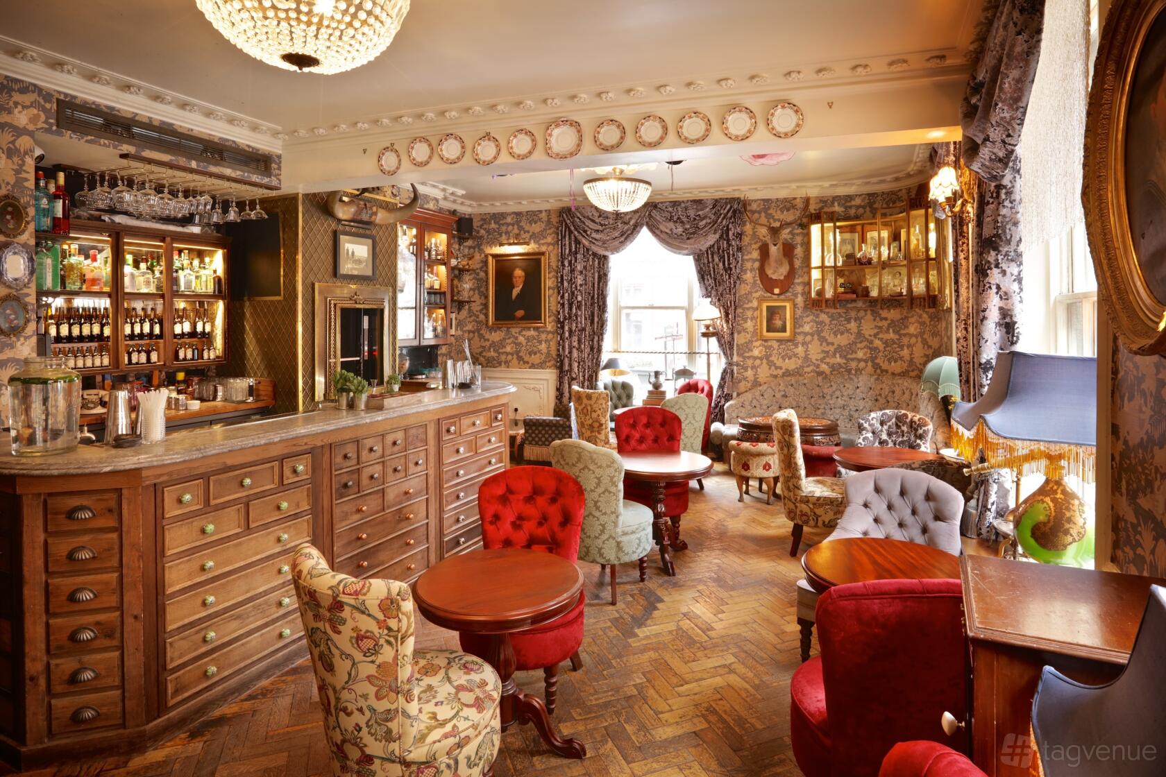A pub with patterned wallpaper, vintage armchairs, ornate décor, and a wooden bar at Mr Fogg's Tavern.