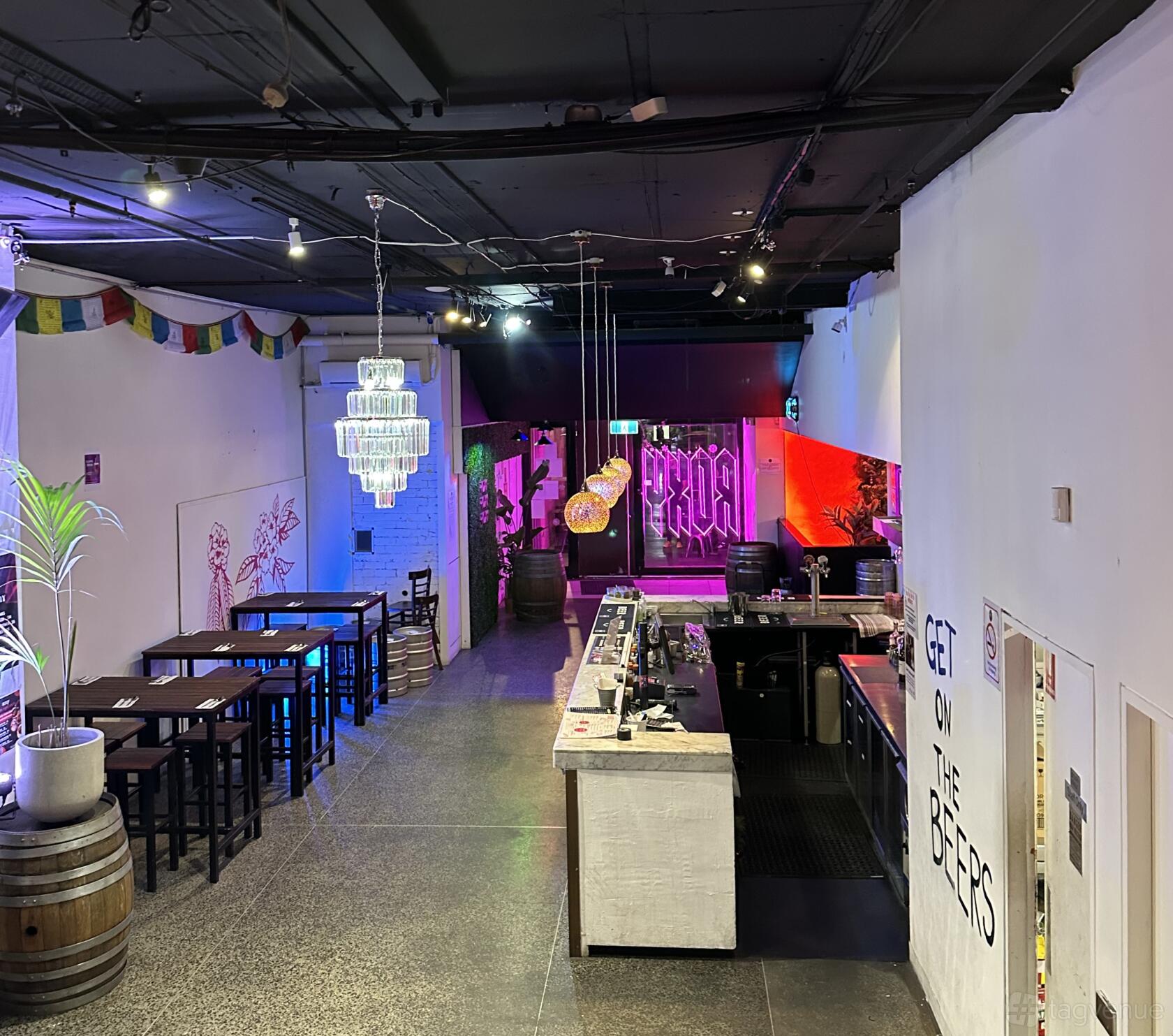 A restaurant with long communal tables, colorful pendant lights, and a central bar at Roxy Kitchen and Bar.