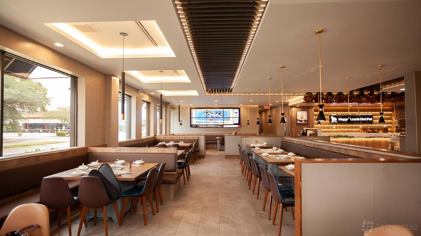 A restaurant with booth seating, neutral tones, large windows, and a digital display at Happy Lamb Hot Pot.