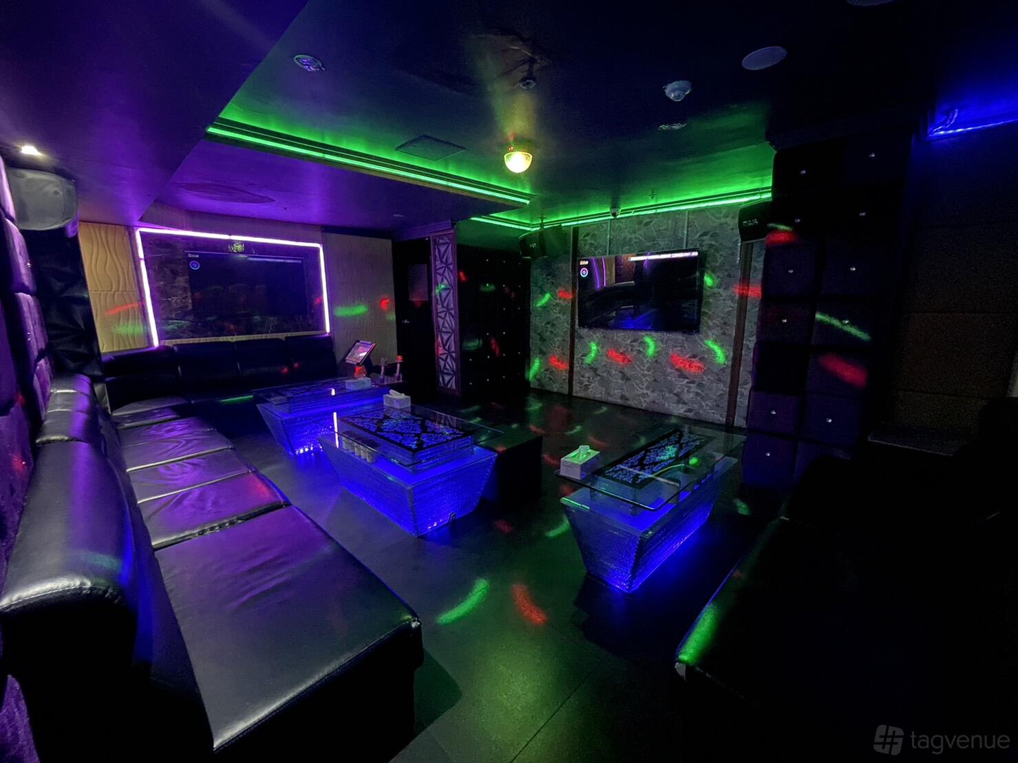 A karaoke bar with long black leather sofas, neon lighting, and a wall-mounted TV at D1 Karaoke Sydney.