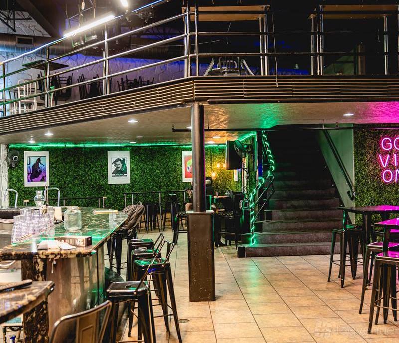 A bar with a marble counter, high stools, neon lighting, framed wall art, and a staircase at Cielo Latin Bar & Grill.