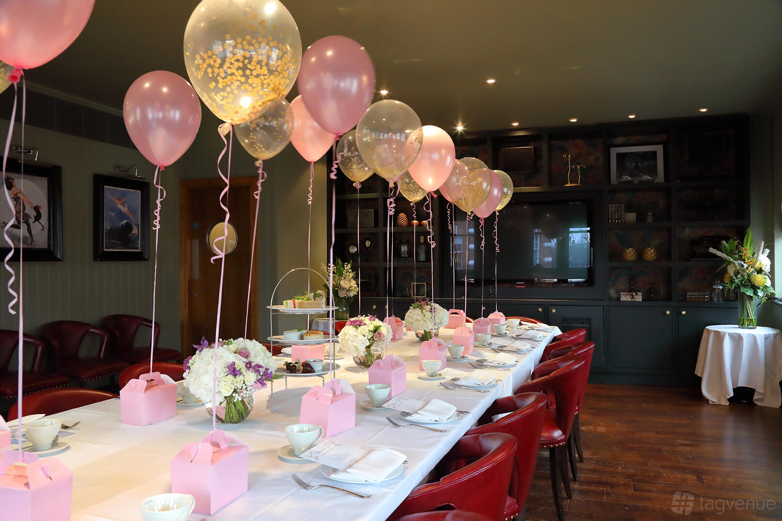 An event space with a long table set with pink gift boxes, floral centerpieces, and pink balloons at Albert's at Beaufort House.
