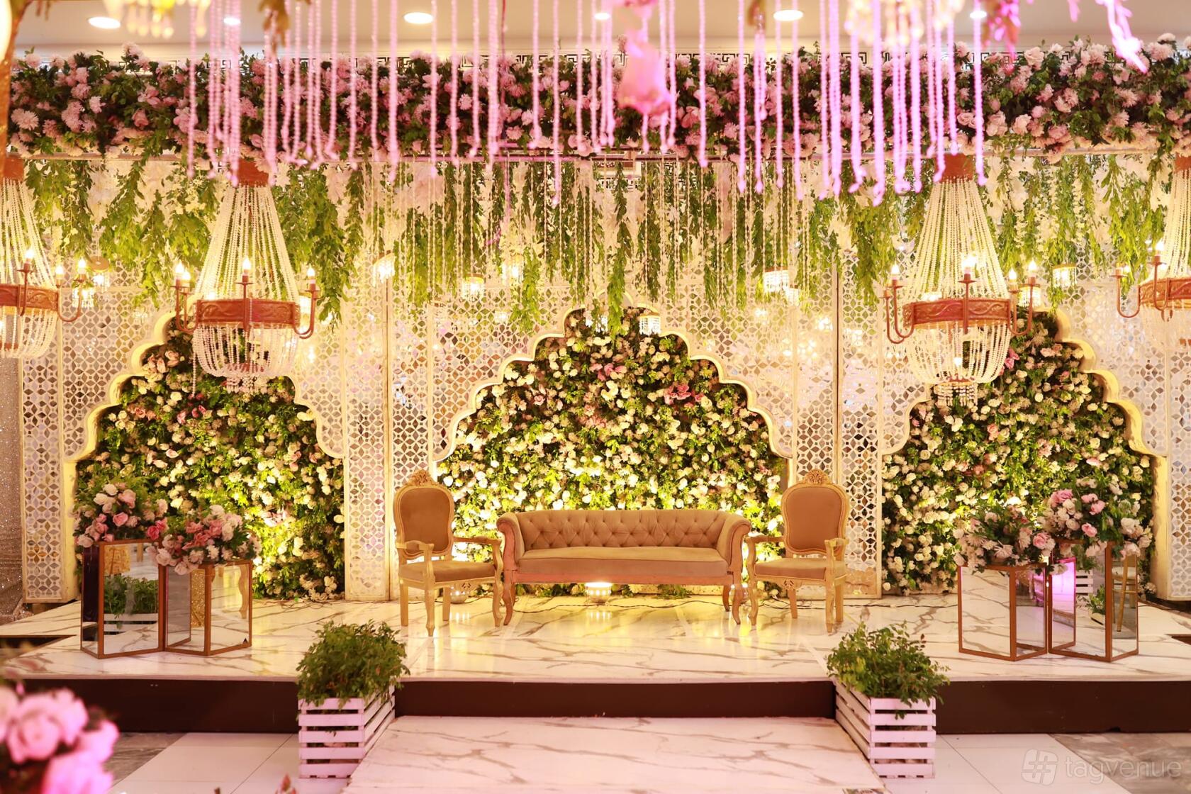 An event venue hall with a floral backdrop, golden chairs, chandeliers, and marble flooring at Excellency Bolton.