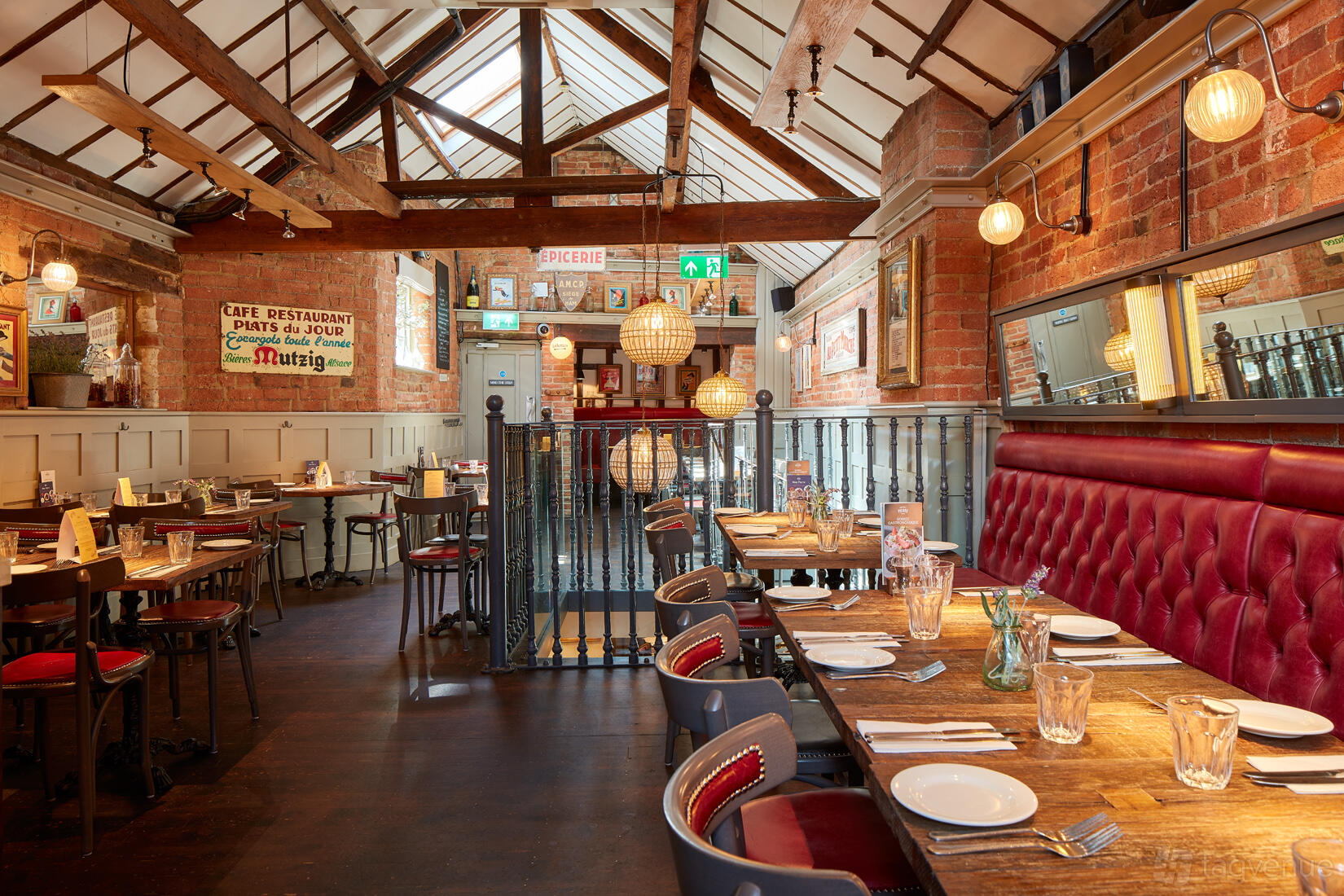 A dining room with exposed brick walls, wooden beams, and red upholstered chairs at Bistrot Pierre Derby.