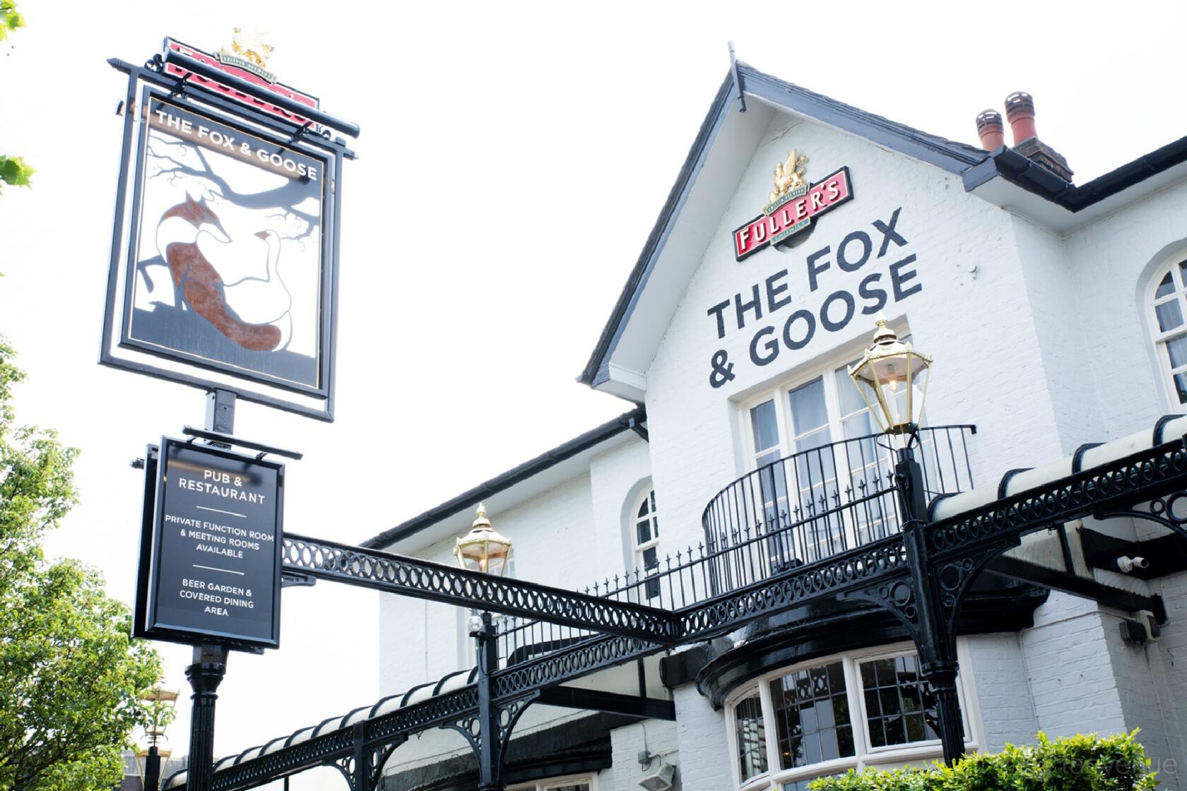 A hotel with a white brick exterior, black railings, and traditional signage at The Fox and Goose Hotel.