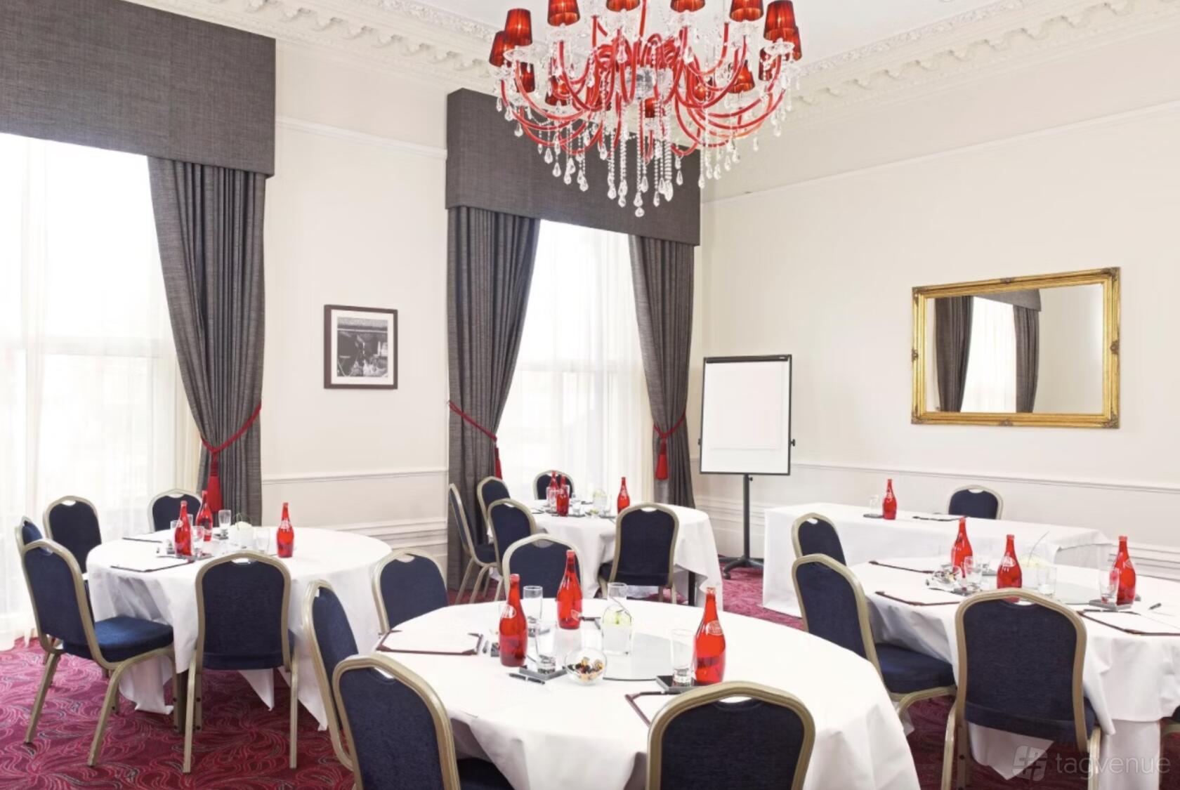 An event space with round tables, red glass chandeliers, and large windows with dark drapes at The Clermont Victoria.