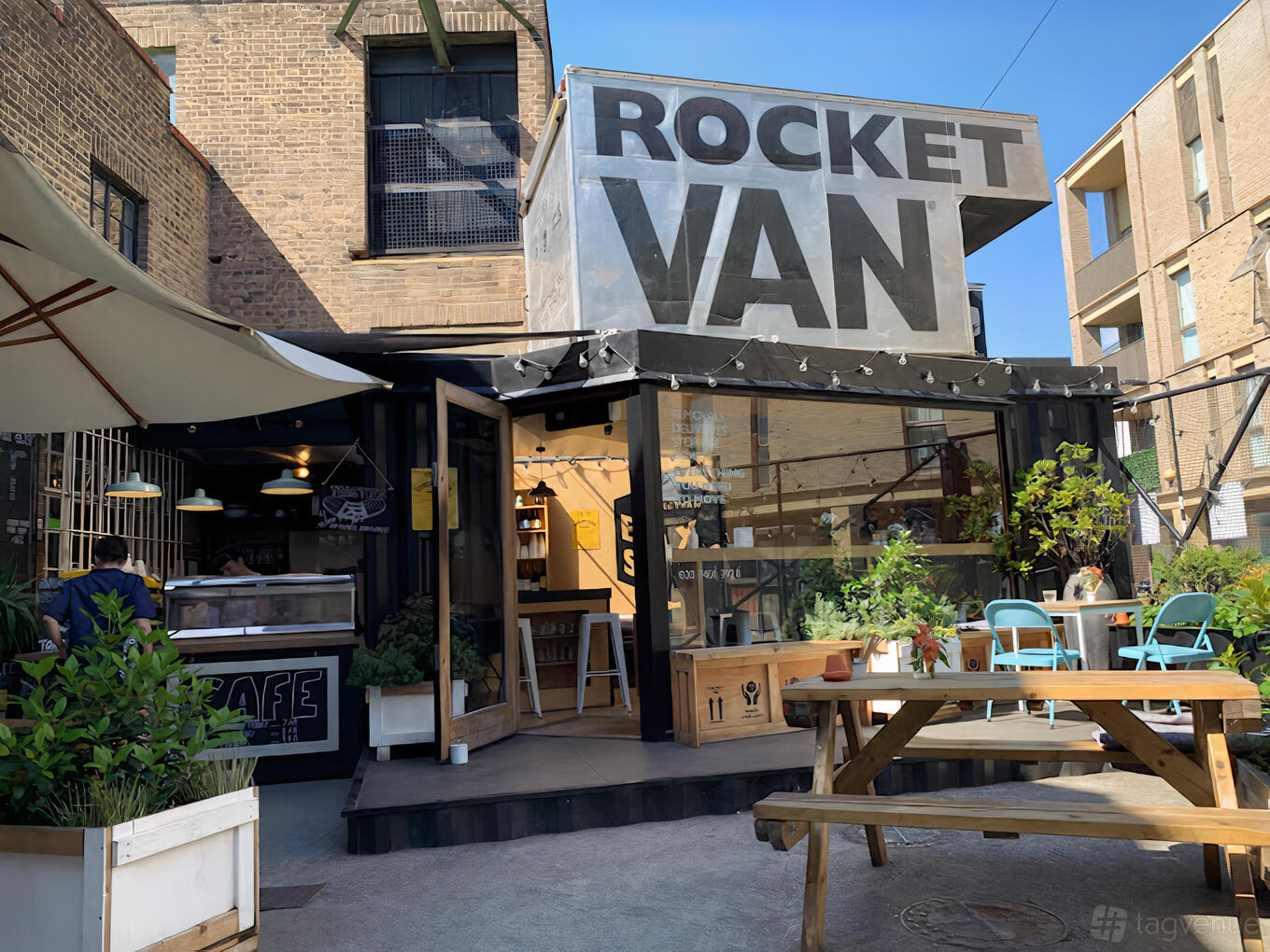 A warehouse venue with glass entry, outdoor seating, picnic tables, and large rooftop signage at Rocketvan.