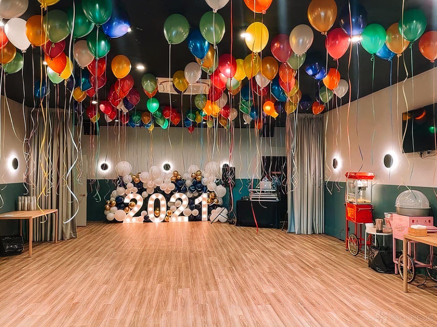 An event venue with colorful balloons hanging from the ceiling, light wood floors, and a popcorn machine at The Deck Brighton Kids