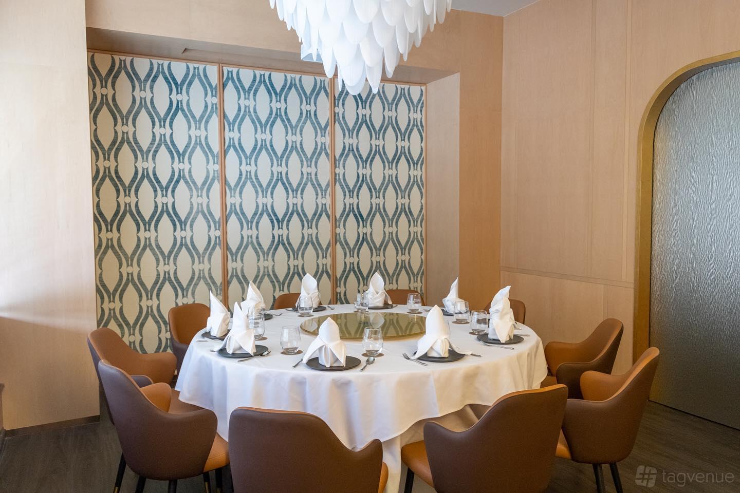 A dining room with a round table set with white linens and napkins, patterned wall panels, and cushioned chairs at SARAI FINE THAI.