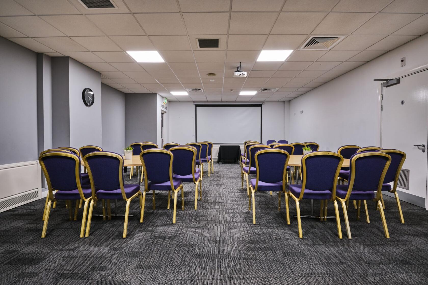 A meeting room with purple chairs arranged in rows facing a projector screen at Swansea.com Stadium.