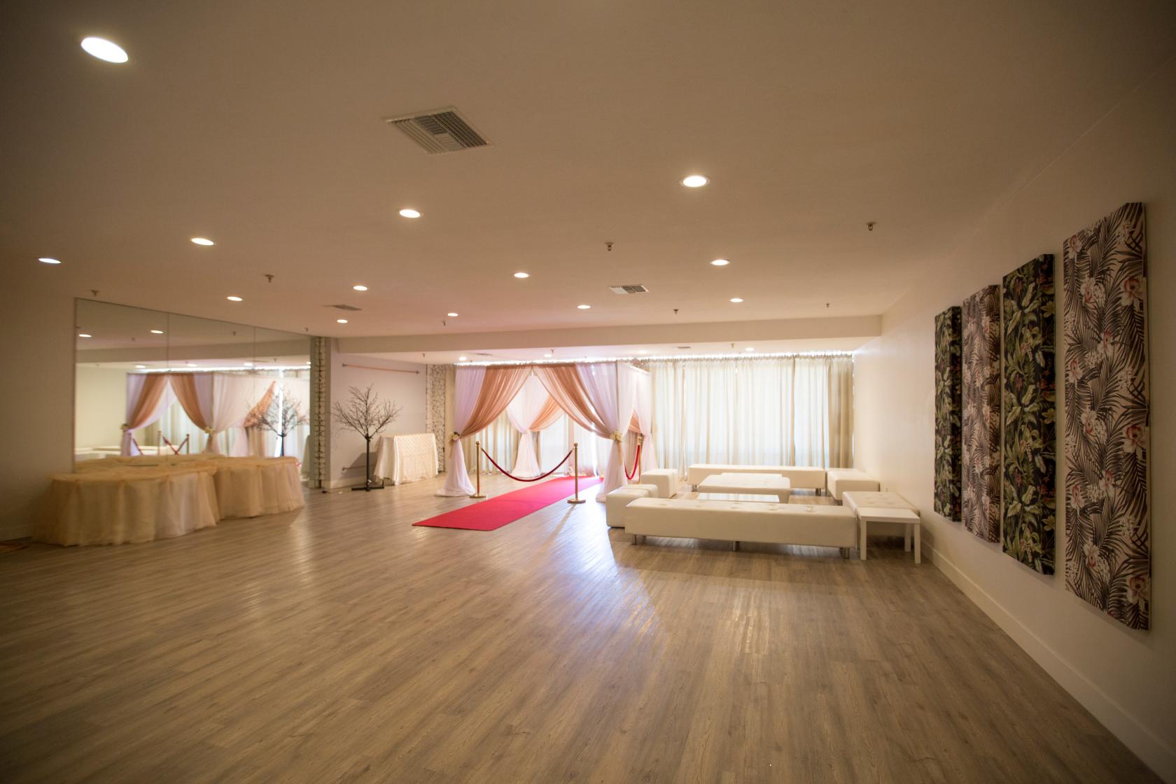 A spacious hall with wood flooring, a red carpet entrance, sheer drapes, and white lounge seating at BLVD Hall.