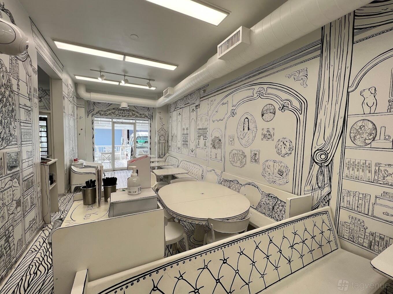 A restaurant with hand-drawn black and white wall art, white tables, and booth seating at 2D Restaurant.