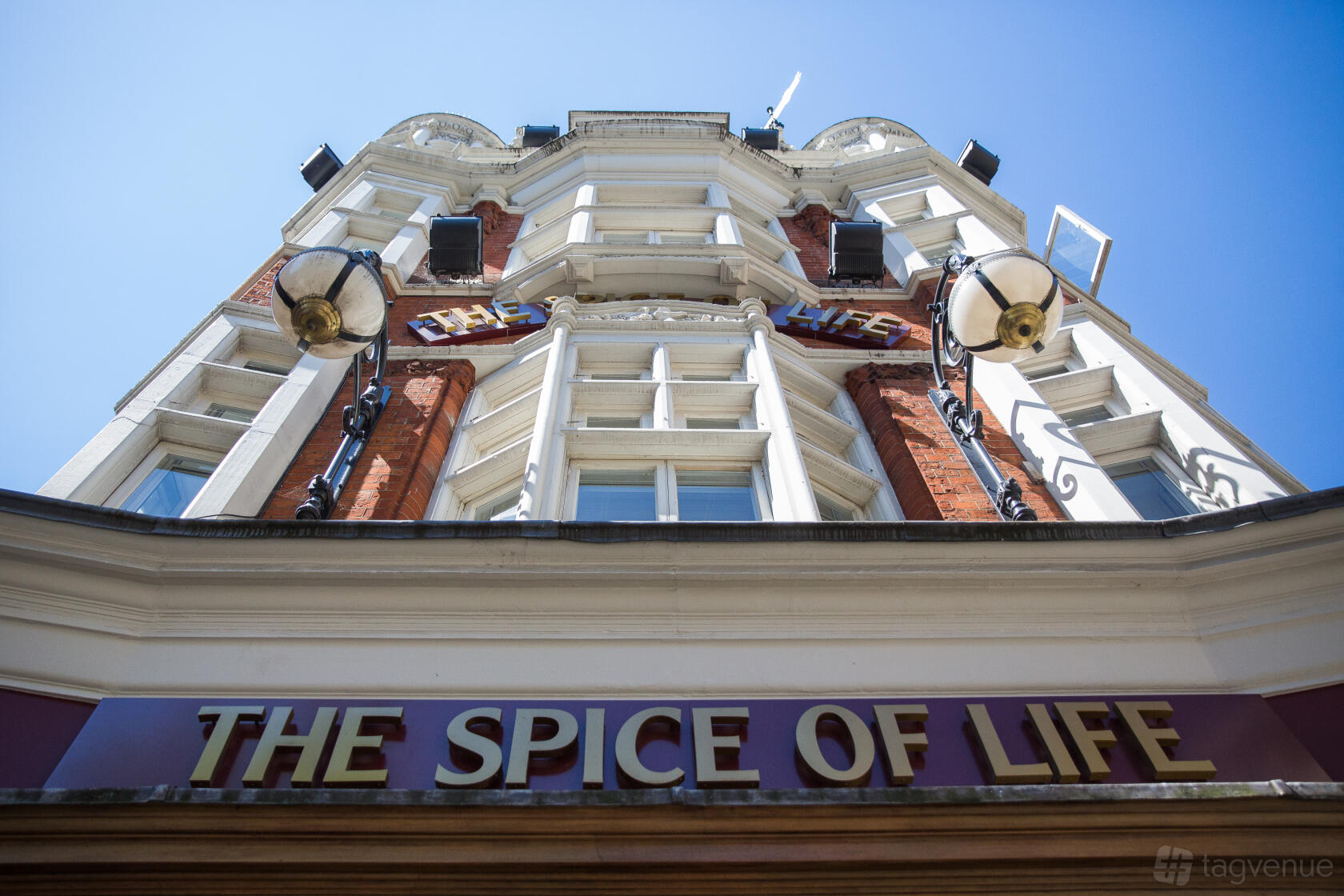 A red brick pub with ornate windows, decorative lamps, and gold signage reading The Spice of Life - Soho.