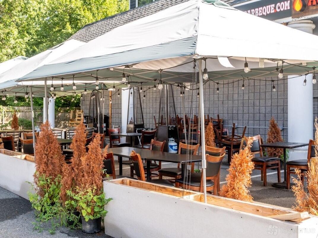 A restaurant terrace with wooden tables, black chairs, tented cover, string lights, and potted plants at Addy's Barbeque.