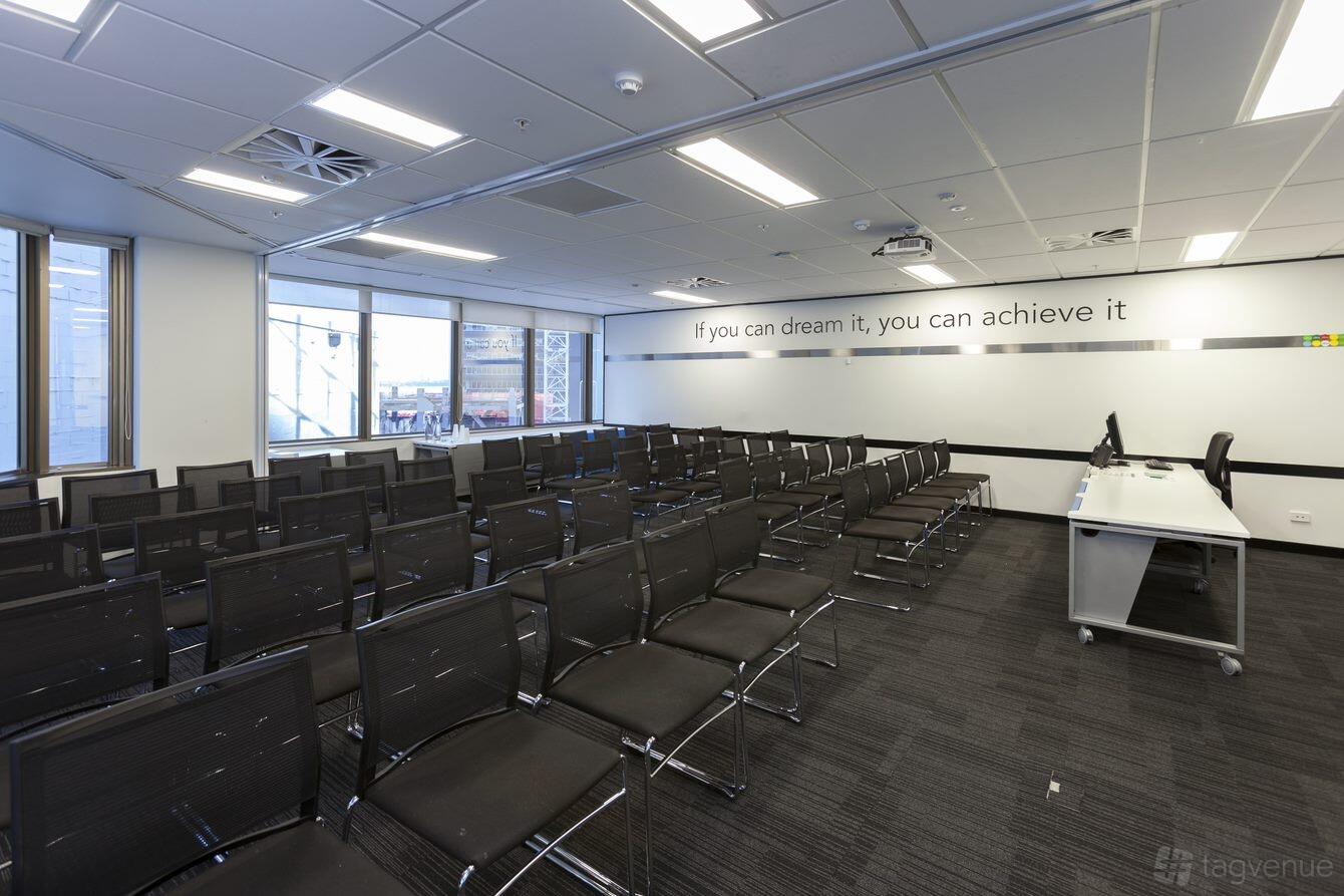 An auditorium with rows of black mesh chairs, large windows, and a whiteboard wall at Cliftons Perth.