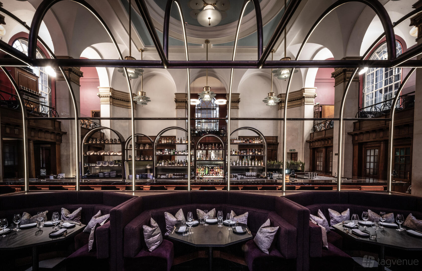 A restaurant mezzanine with curved banquette seating, arched windows, and a view of the bar at Lucky Cat - Manchester.