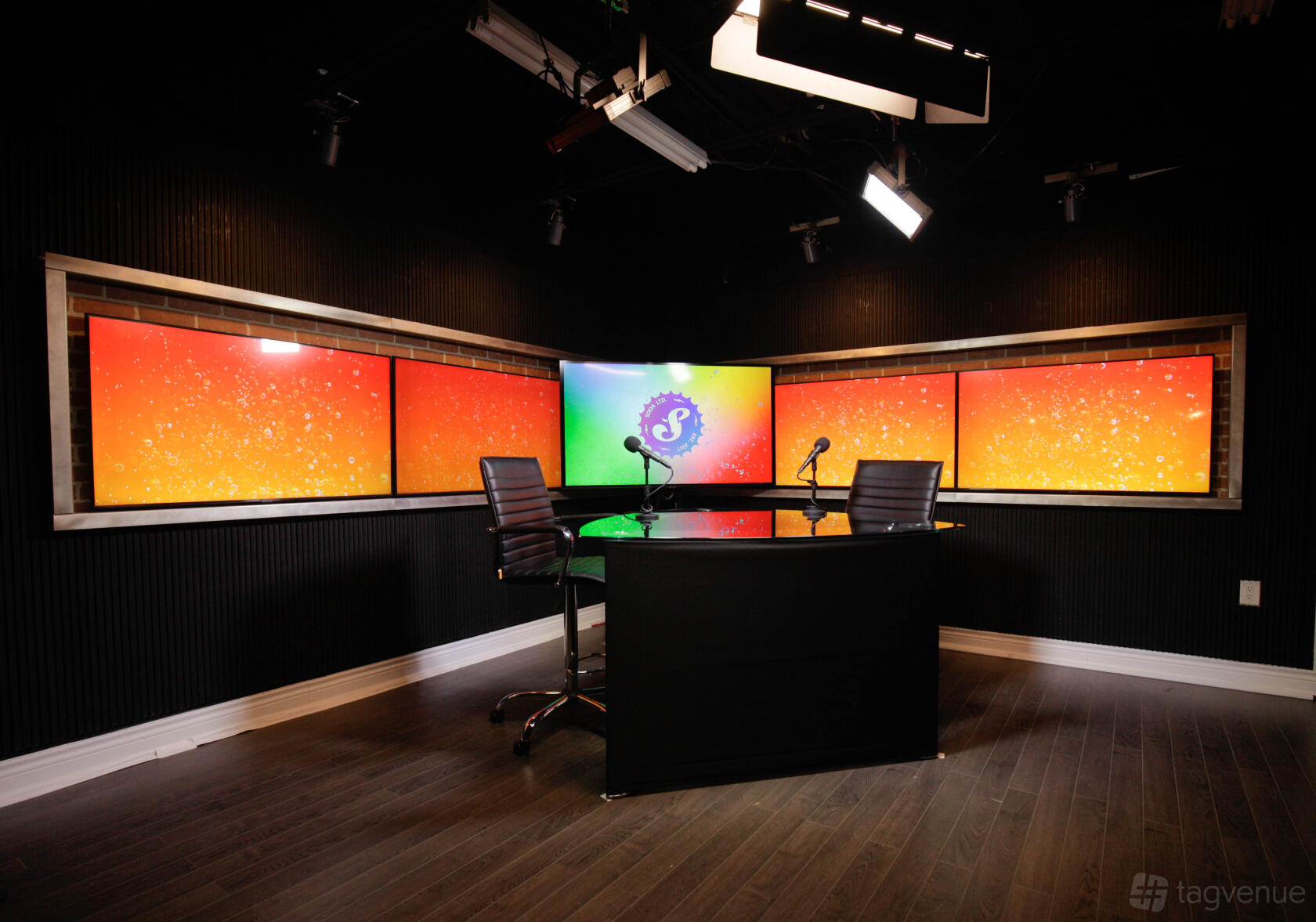 A recording studio with a glass table, two microphones, and colorful wall-mounted screens at Soda Studio.