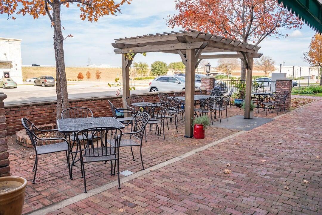 An outdoor patio with metal tables and chairs, brick flooring, and a wooden pergola at Apollonia's Italian Kitchen.