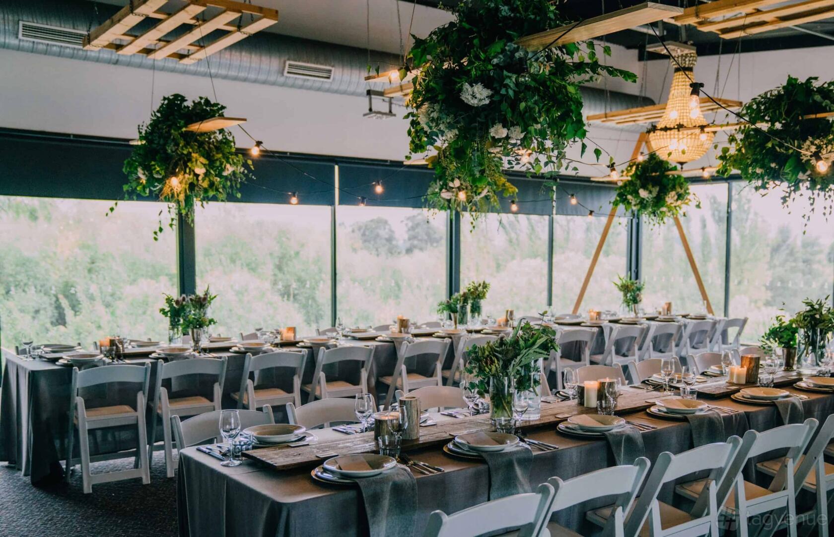 An event venue with long banquet tables, hanging greenery, and floor-to-ceiling windows at Tailrace Centre.