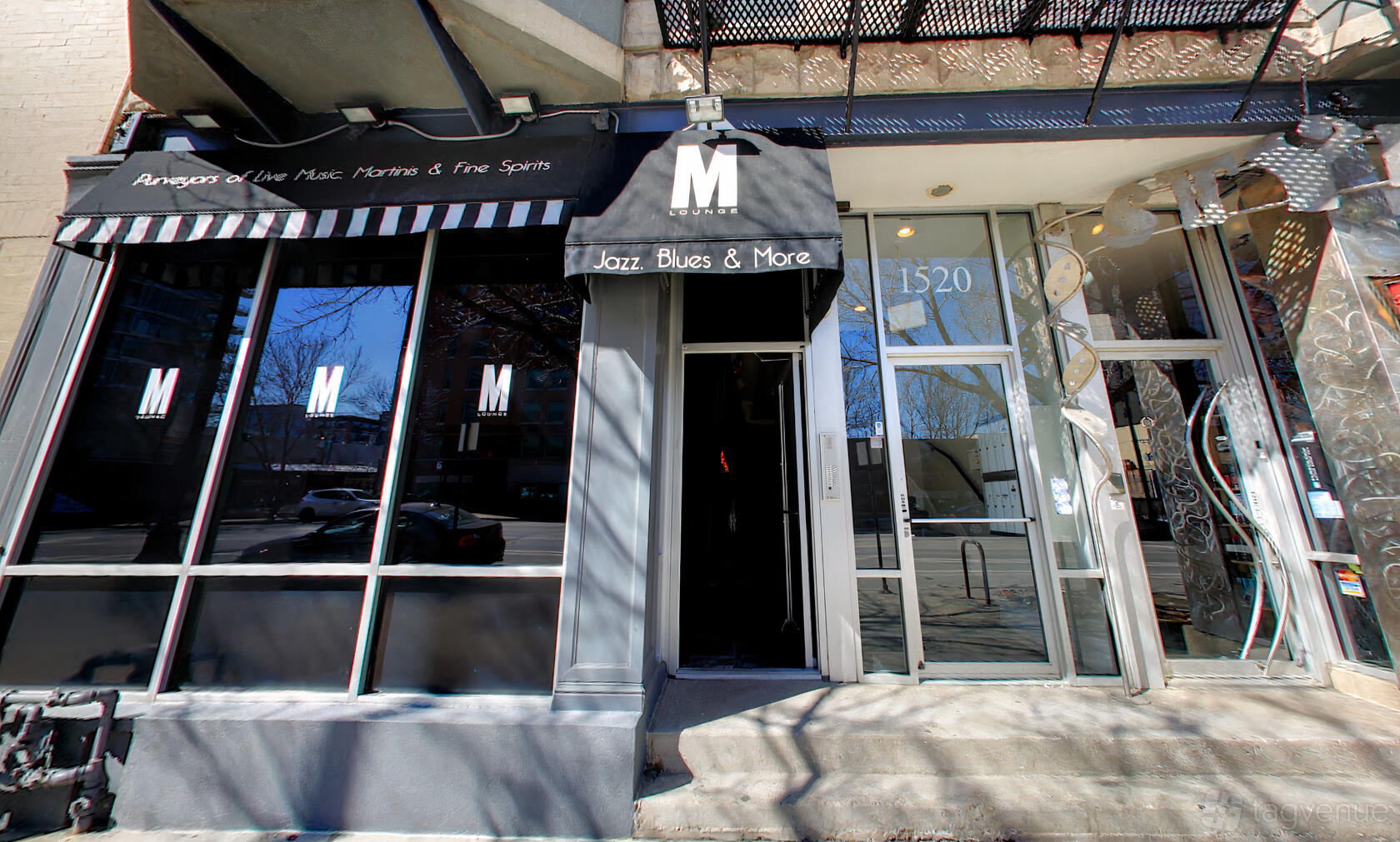 A bar entrance with black striped awning, signage for live music and martinis at M Lounge.