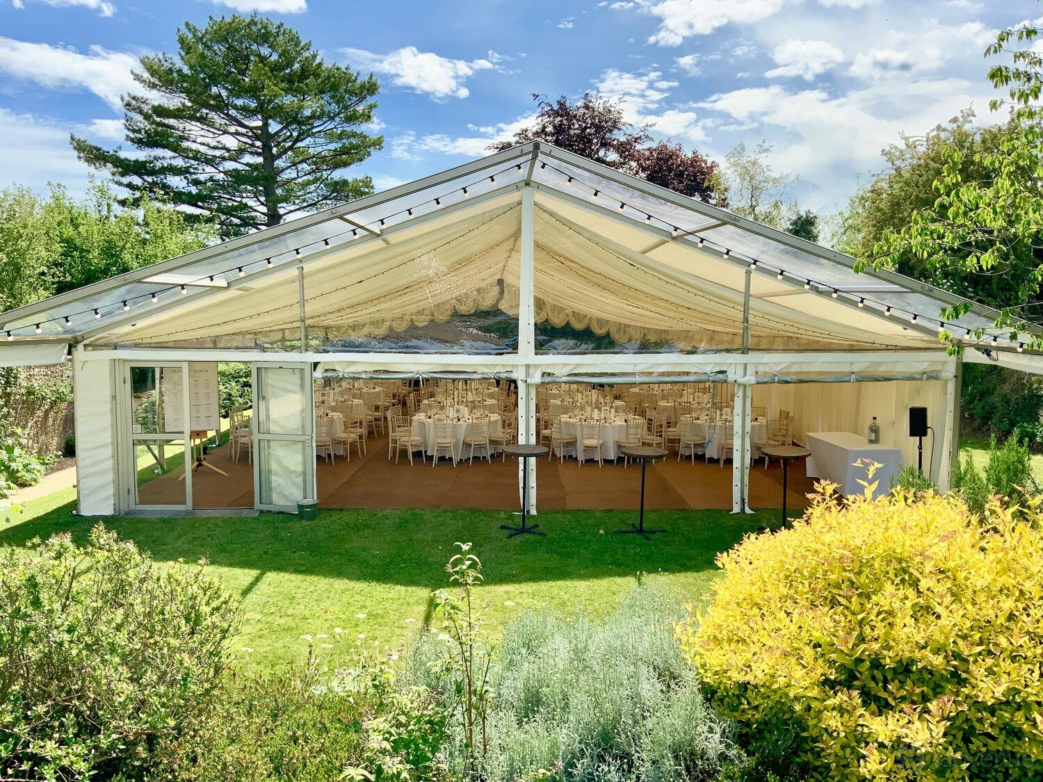 An outdoor event marquee with clear sides, cream draping, and round tables set for dining at Hamswell House.