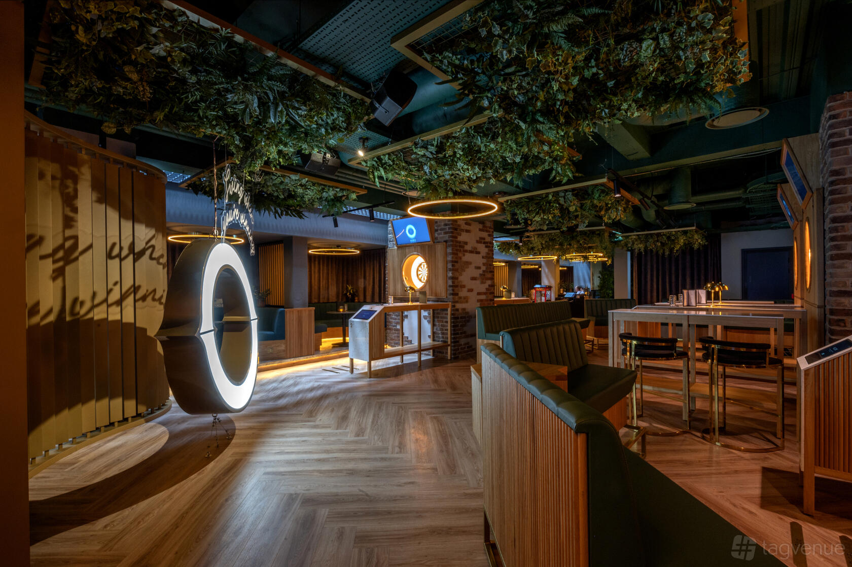 An event space with semi-private booths, greenery on the ceiling, ring lights, and wooden flooring at Oche.