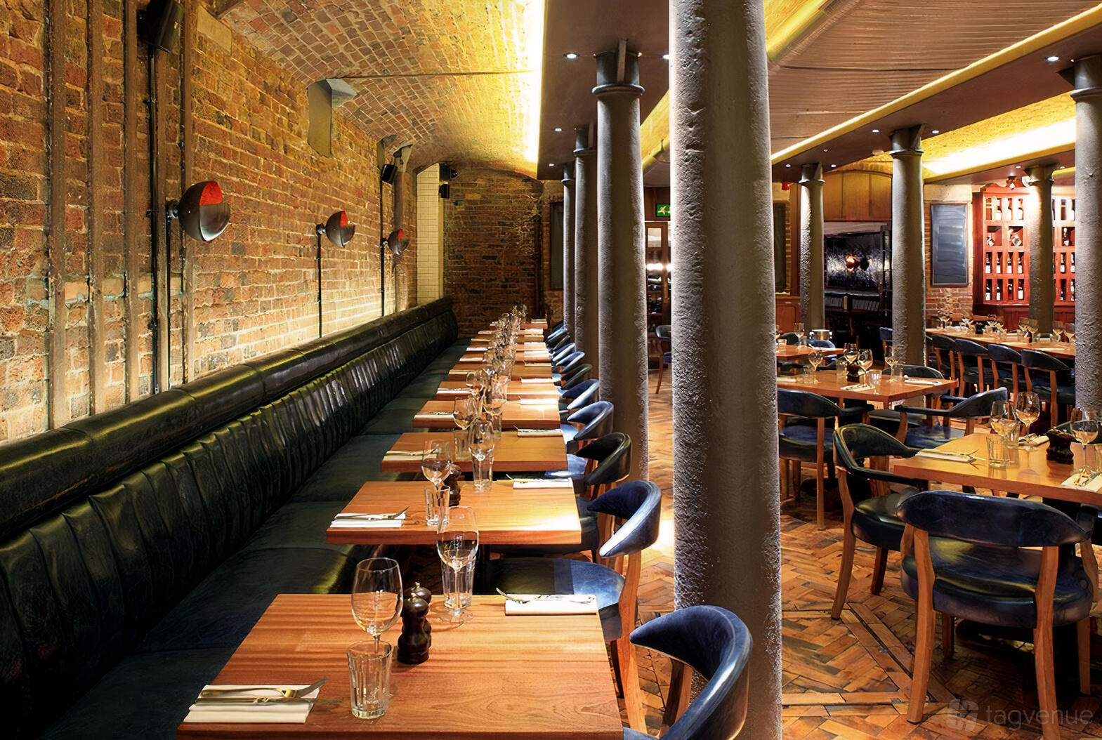 A restaurant with exposed brick walls, leather banquette seating, and wooden tables at Hawksmoor Seven Dials.