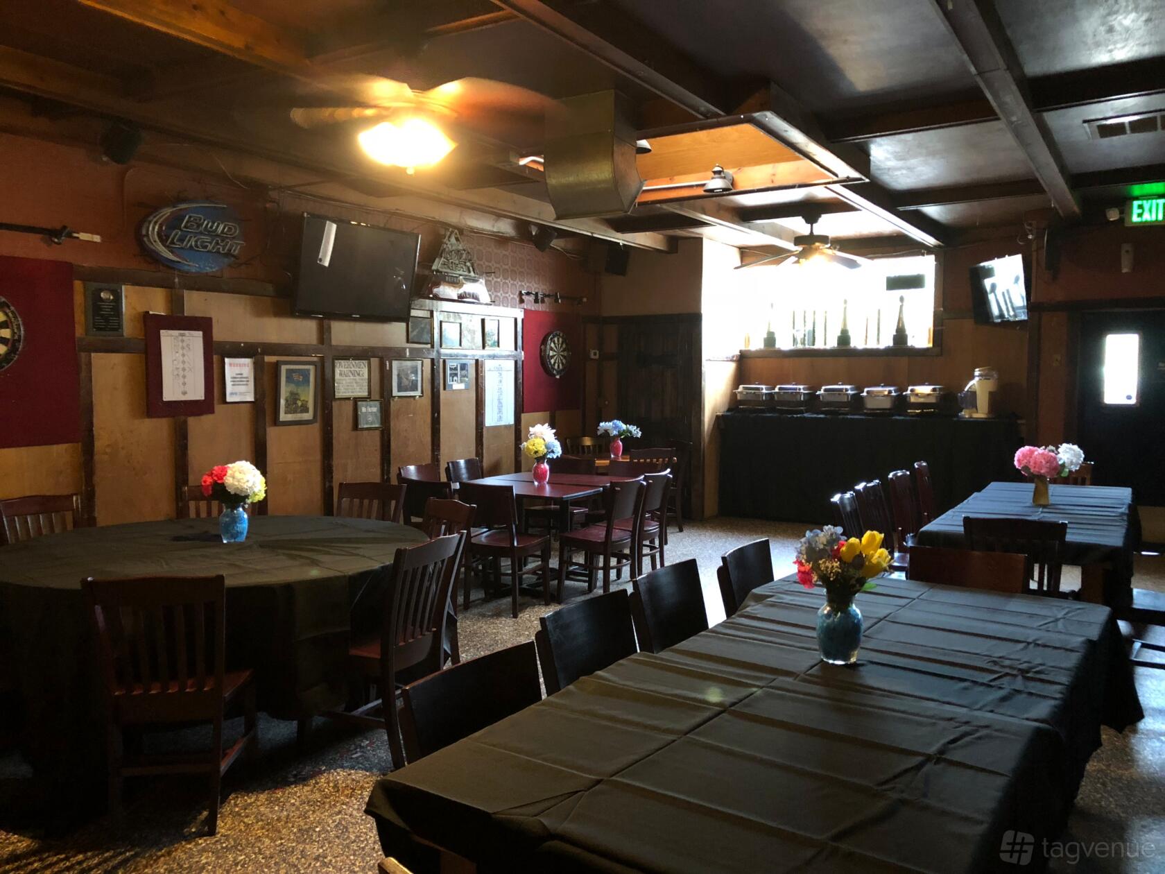 A pub with dark wood tables, black tablecloths, wall-mounted TVs, dartboards, and buffet setup at The Gather Inn Again.