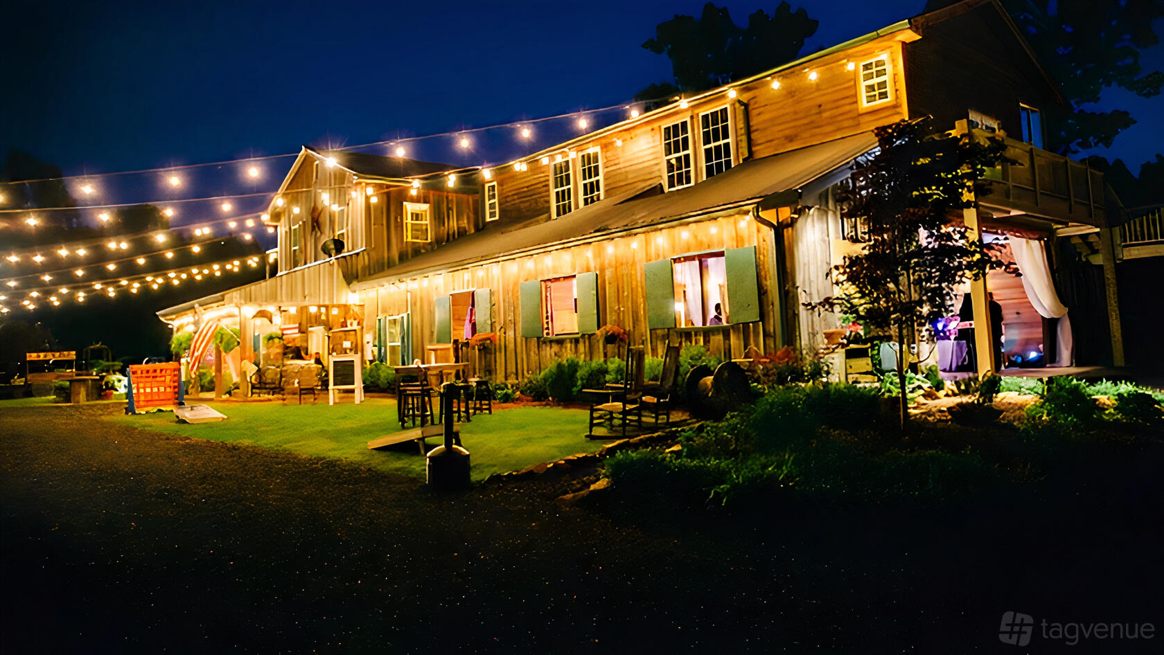 A barn venue with string lights, wooden siding, and rocking chairs on a grassy patio at Cold Creek Farm.