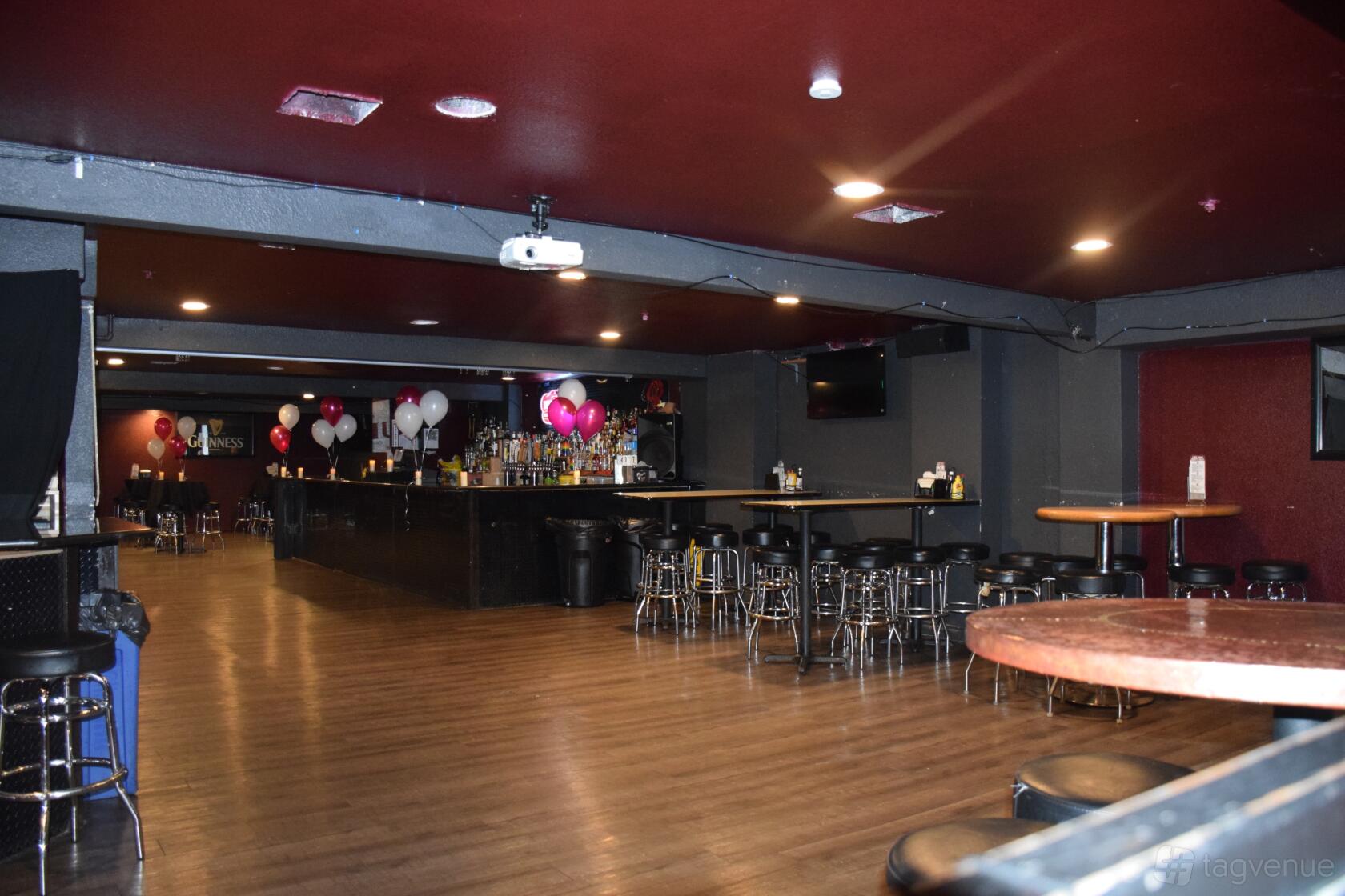 An event space with a wooden floor, central bar, and tables with stools at Ozzie's in Seattle.
