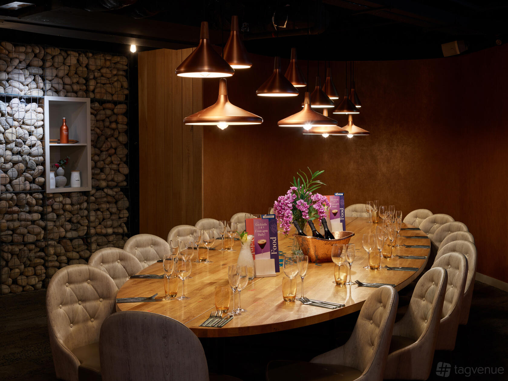 A dining room with a long wooden table, tufted chairs, copper pendant lights, and floral centerpiece at Banyan Corn Exchange.