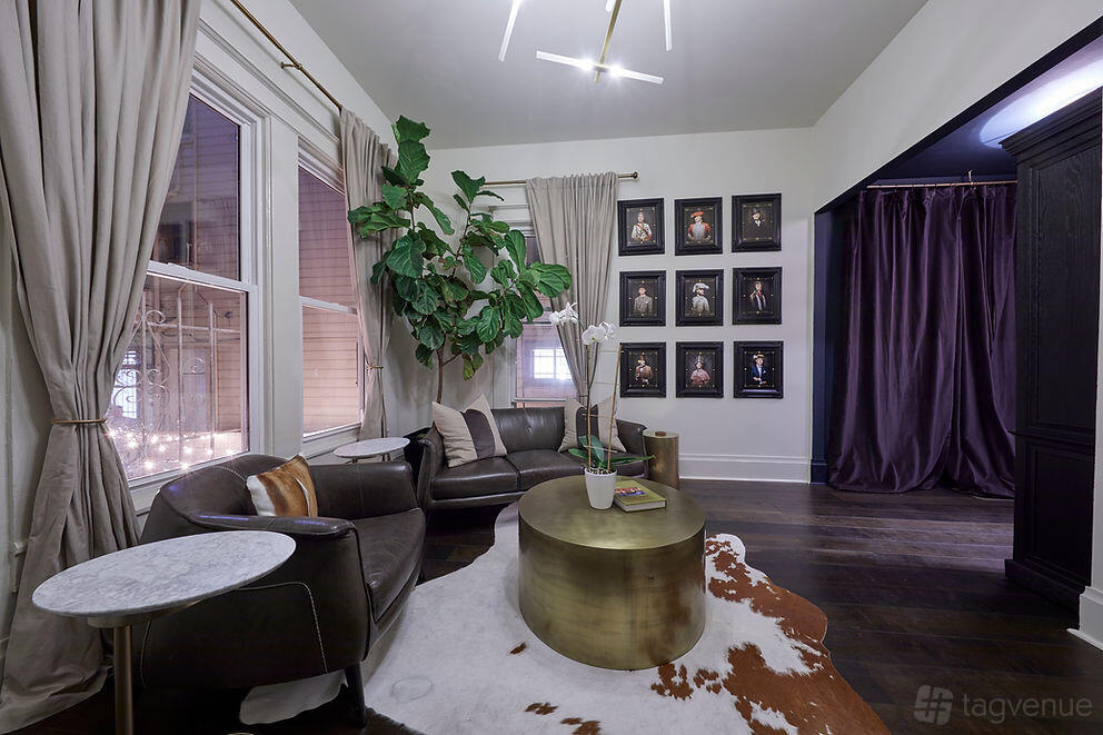 A bar lounge with leather armchairs, a round gold coffee table, floor-to-ceiling curtains, and framed portraits at The Academy