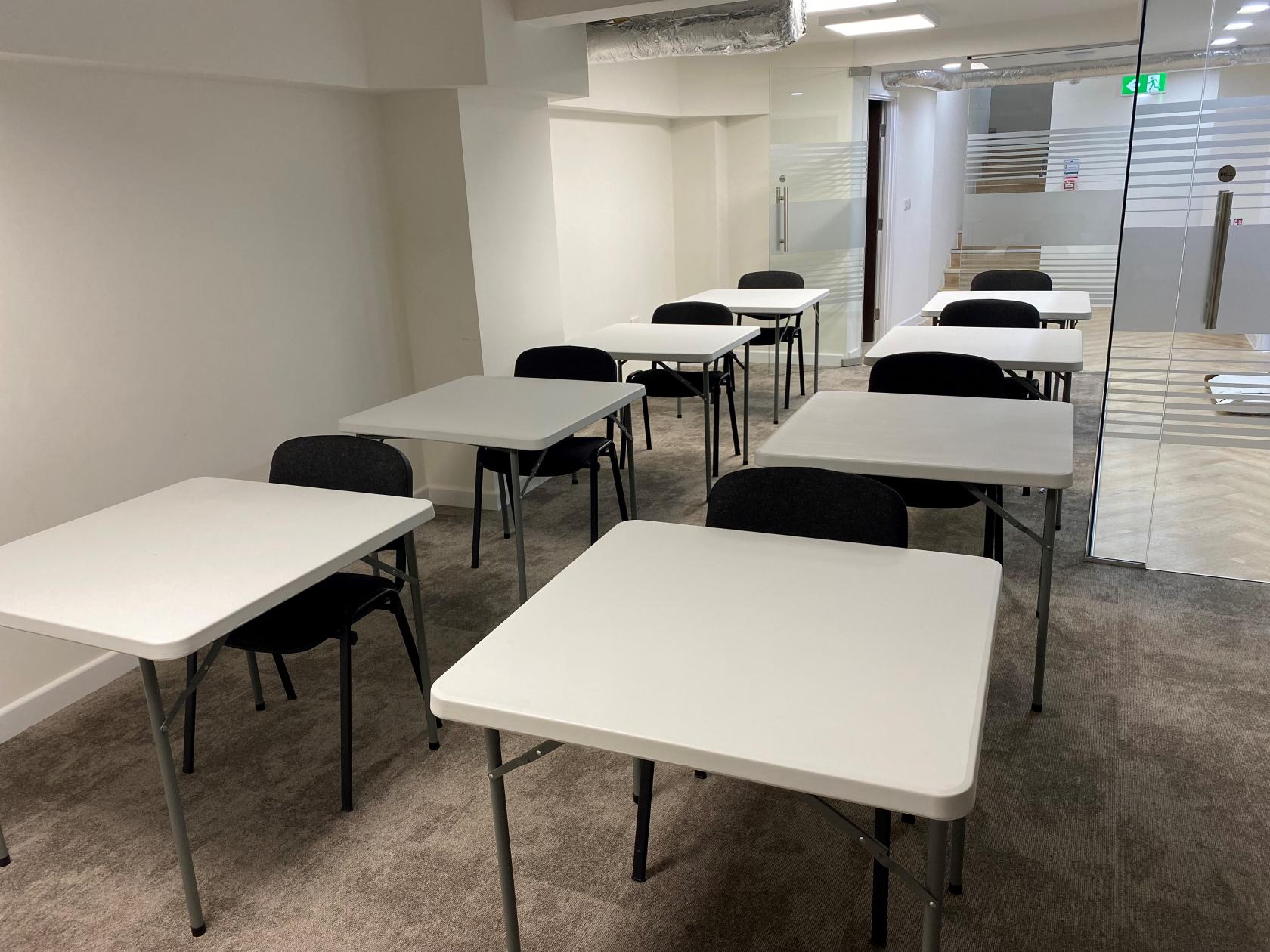 A meeting room with white rectangular tables, black chairs, and glass doors at W Dental.
