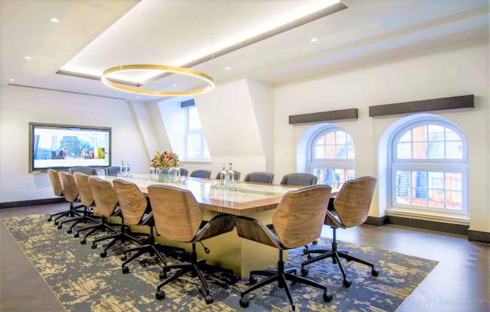 A meeting room with a large wooden conference table, ergonomic chairs, and arched windows at 20 North Audley Street.