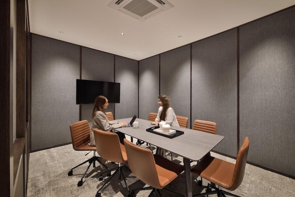 A boardroom with a rectangular table, tan leather chairs, grey acoustic wall panels, and a wall-mounted TV at The Great Room - South Bridge.