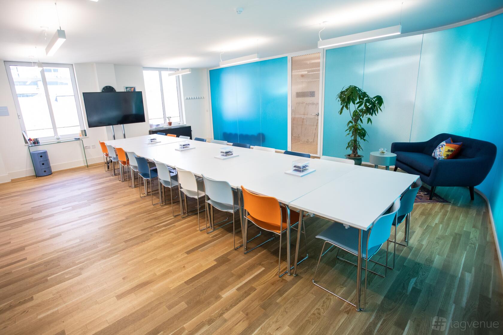 A meeting room with large windows, blue accent wall, modular tables, colorful chairs, and a sofa at Wallacespace Spitalfields.
