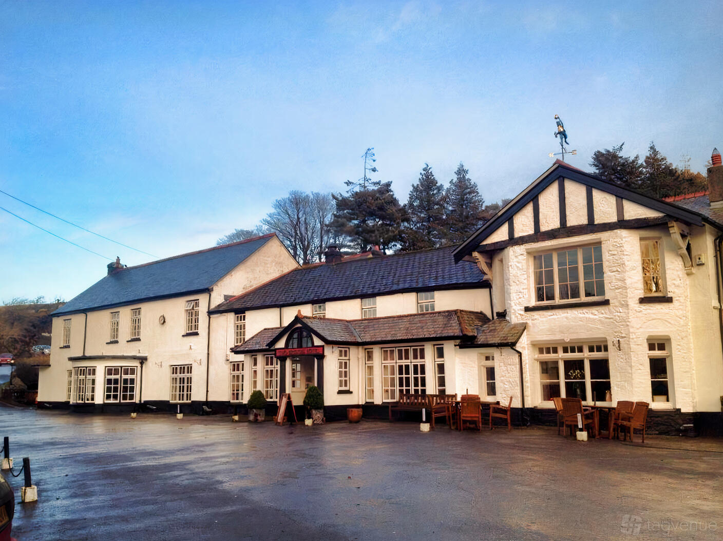 A traditional hotel with white-painted exterior walls, black trim, and outdoor wooden seating at Two Bridges Hotel.