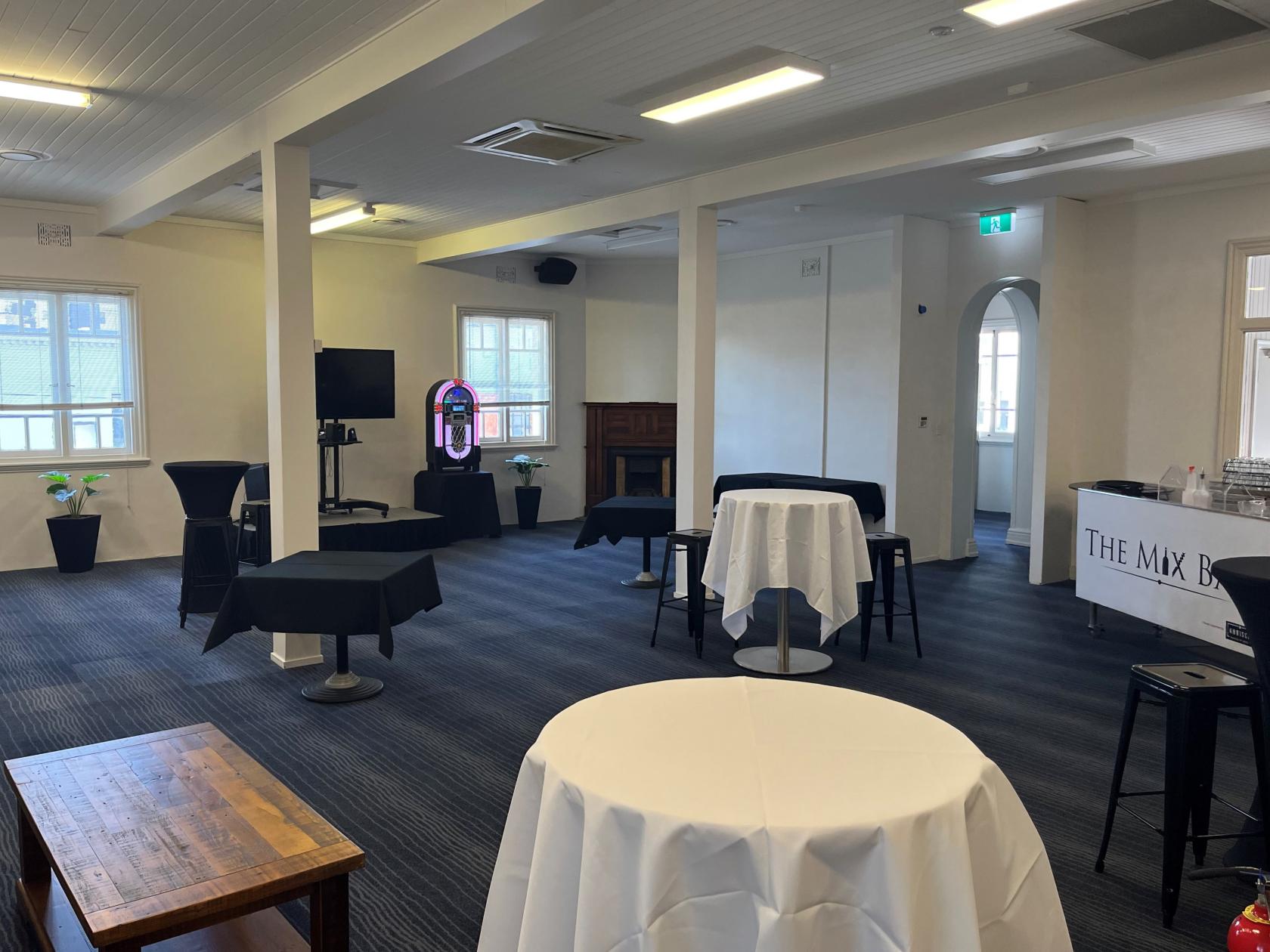 An event space with tall cocktail tables with white linens, windows, and a jukebox at The Mix Bar.