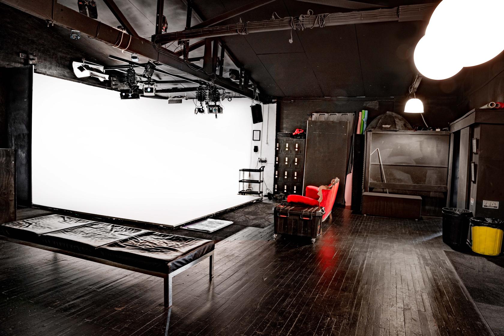 A photo studio with a large white cyclorama wall, black floors, and overhead lighting at Good Loco.